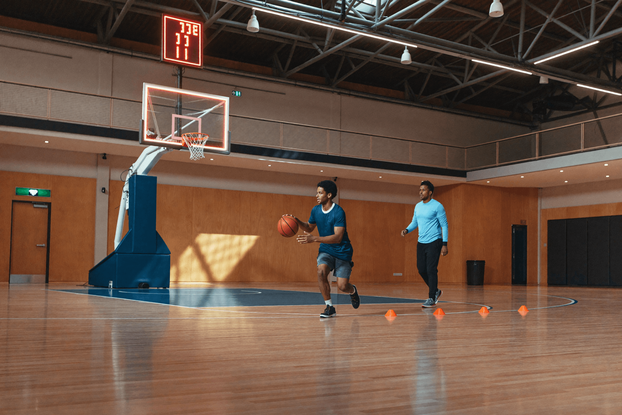 A coach guiding a young athlete through a training drill on an indoor court